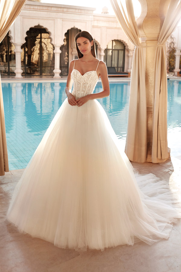 Eine lächelnde Frau im eleganten weißen Brautkleid steht vor einem Pool