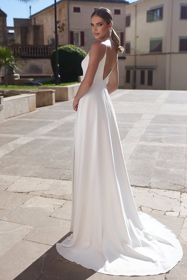 Eine junge Frau mit ernstem Blick trägt ein elegantes weißes Kleid im Sonnenschein