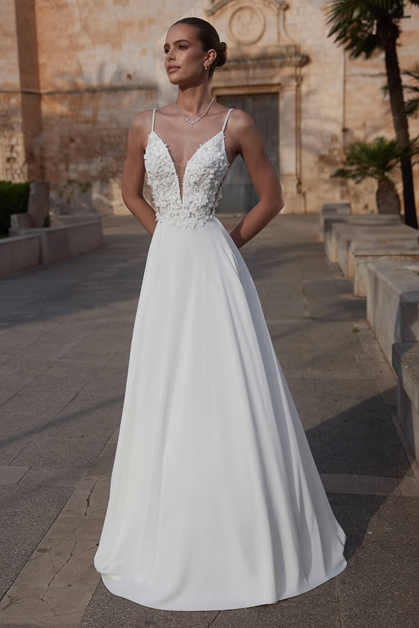 Eine elegante Frau im weißen Brautkleid mit floralen Verzierungen und stolzem Blick