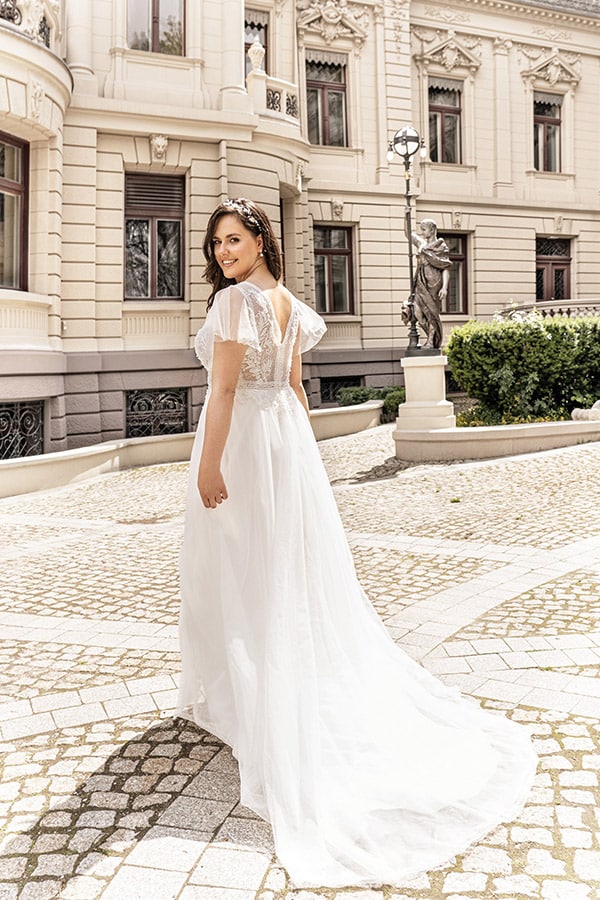 Eine junge Frau im weißen Hochzeitskleid lächelt vor einem historischen Gebäude