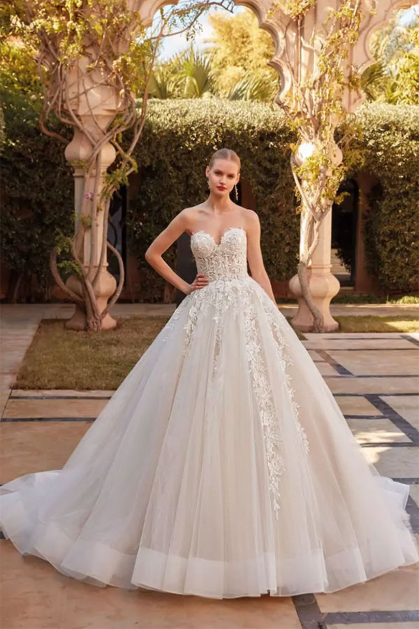 Eine blonde Frau mit ernstem Blick trägt ein elegantes weißes Brautkleid mit Stickerei