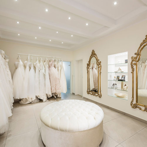 Elegantes Ankleidezimmer mit weißen Brautkleidern, goldenen Spiegeln und Cremefarben