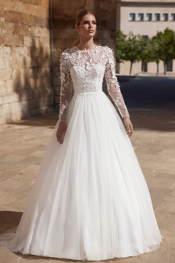 Eine lächelnde Frau trägt ein elegantes weißes Brautkleid mit Spitzenärmeln