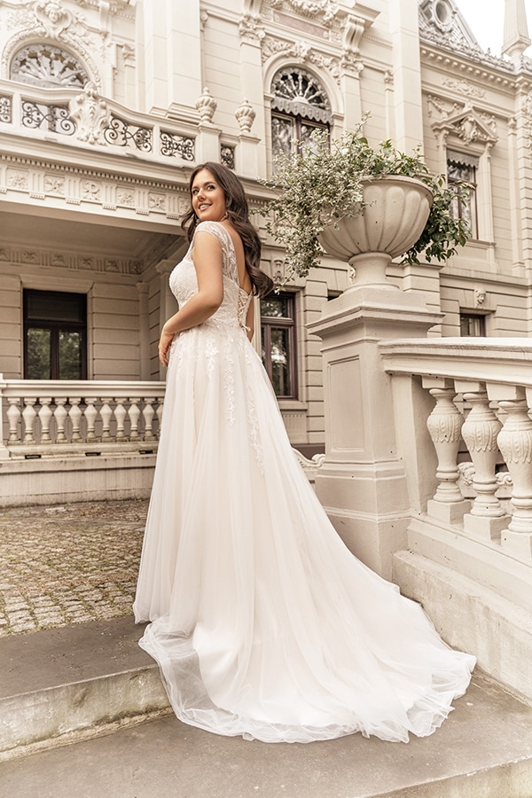 Eine lächelnde Frau im weißen Brautkleid steht vor einem prunkvollen Gebäude