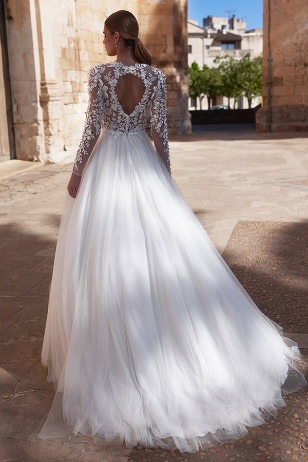 Eine Frau in weißem Spitzenkleid mit Herzausschnitt am Rücken steht vor alten Gemäuern