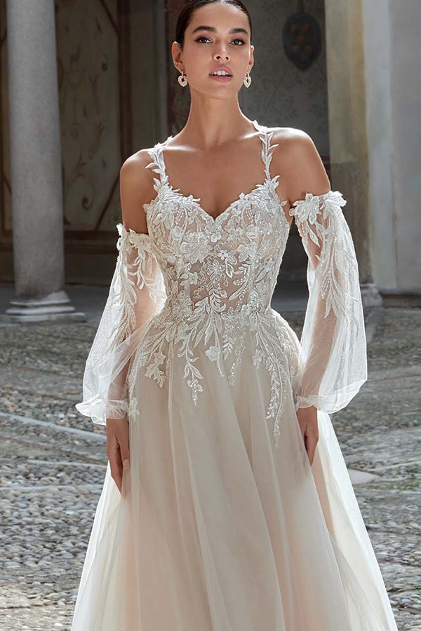 Junge Frau mit ernstem Blick trägt ein weißes Spitzenkleid mit transparenten Ärmeln