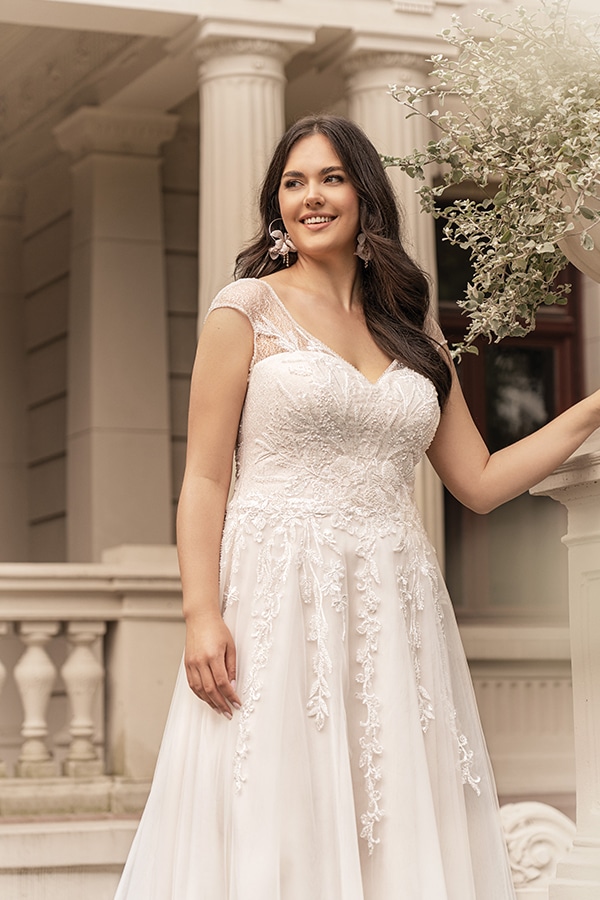 Frau mit langen dunklen Haaren lächelt in eleganter weißer Spitzenrobe vor Säulen