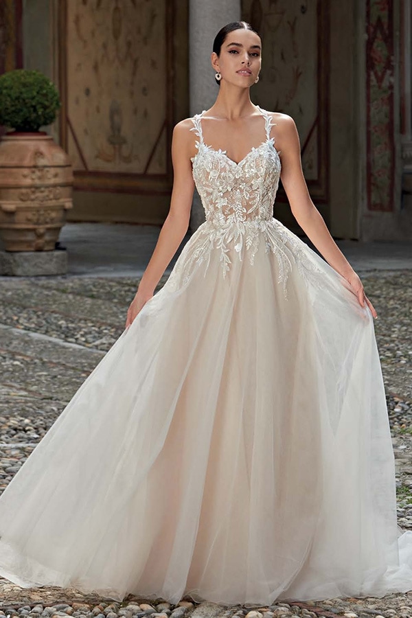 Junge Frau mit ernstem Blick trägt ein cremefarbenes Brautkleid mit floralen Details