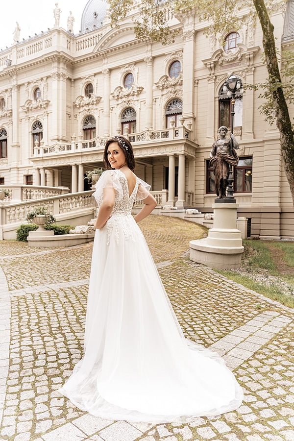Eine lächelnde Frau im eleganten weißen Brautkleid steht vor einem prächtigen Gebäude