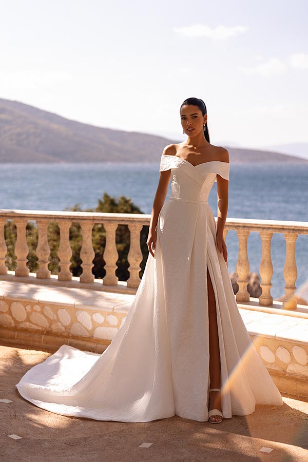 Junge Frau mit elegantem weißen Brautkleid, ernstem Blick und Meereskulisse