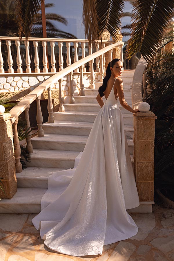 Eine Frau im weißen Brautkleid blickt ernst auf einer sonnigen Marmortreppe zurück