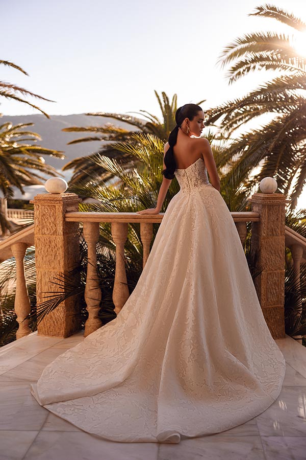 Eine Frau im eleganten cremefarbenen Brautkleid steht nachdenklich auf einer Terrasse