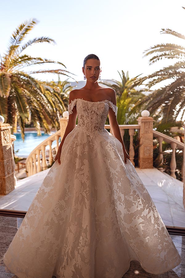 Junge Frau im cremefarbenen Brautkleid mit floralen Mustern steht vor Palmen