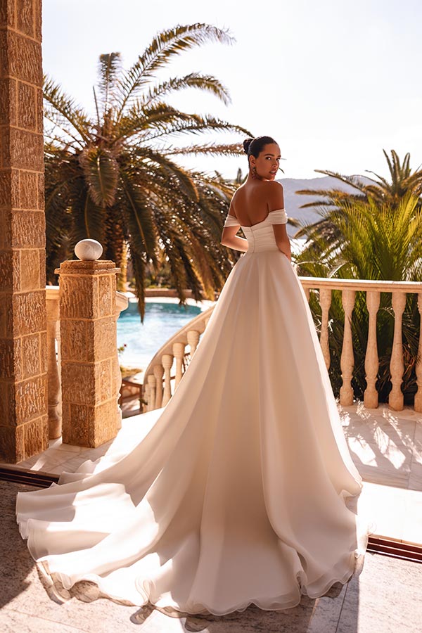 Eine elegant gekleidete Frau im weißen Brautkleid steht auf einem sonnigen Balkon