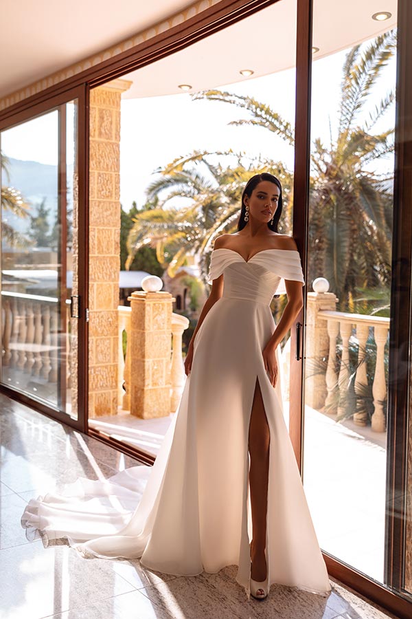 Frau im eleganten weißen Kleid mit Schlitz und selbstbewusstem Blick am Fenster