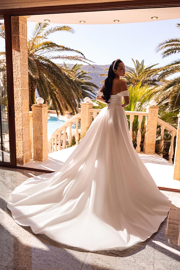 Eine Frau im eleganten weißen Brautkleid steht lächelnd auf einer sonnigen Terrasse