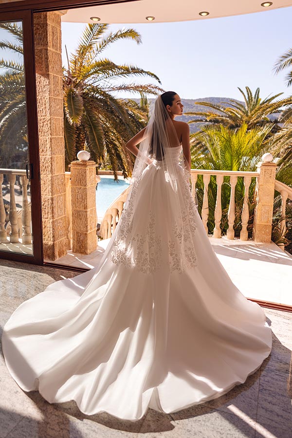 Eine Frau im eleganten weißen Brautkleid mit Schleier blickt auf Palmen und Pool