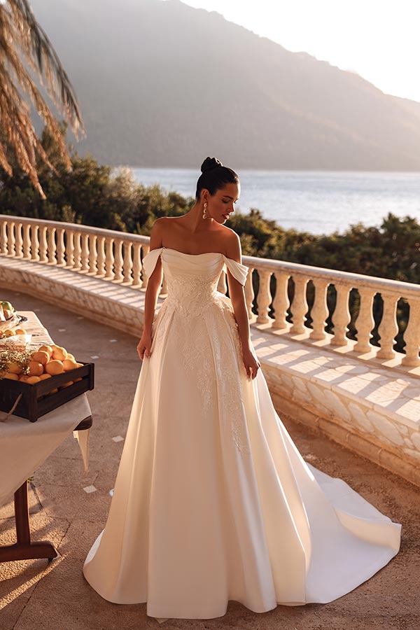 Eine elegant gekleidete Frau im Brautkleid steht lächelnd auf einer Terrasse am Meer