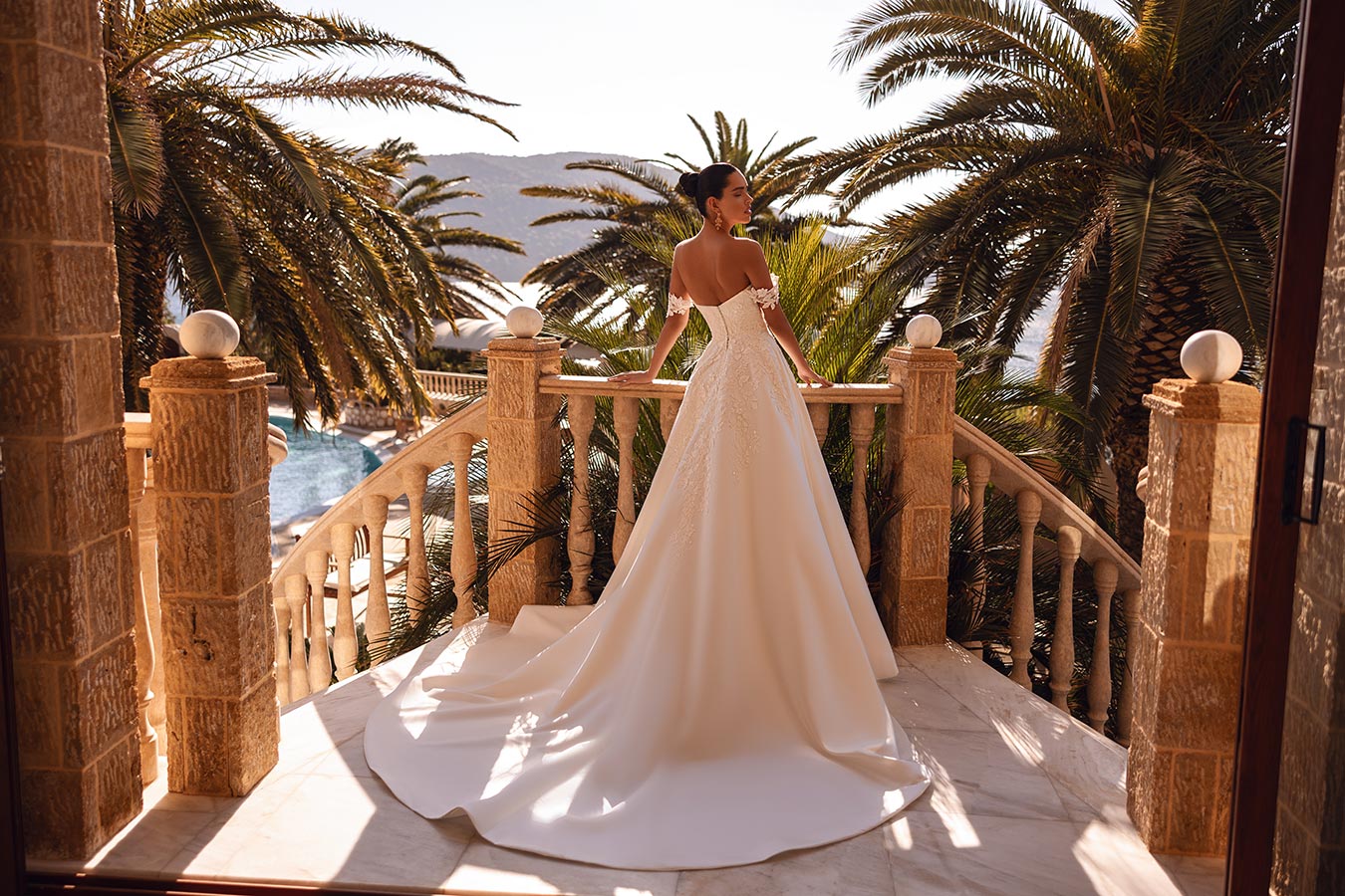 Eine Frau im eleganten weißen Brautkleid steht auf einem sonnigen Balkon mit Palmen