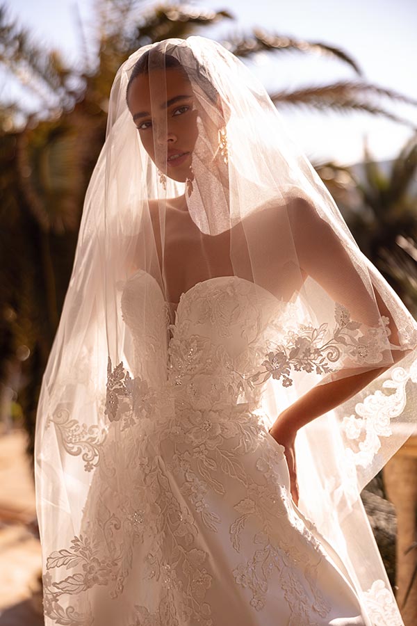 Eine Frau in einem eleganten weißen Brautkleid steht nachdenklich im Sonnenschein