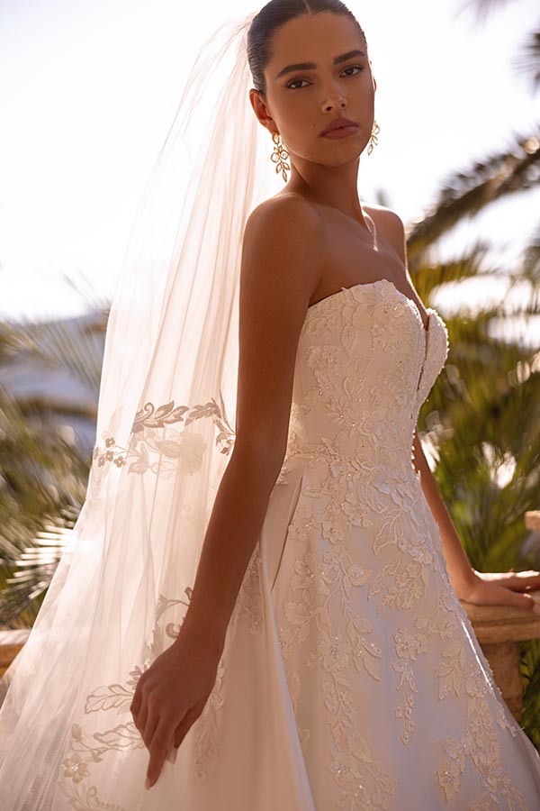 Junge Frau in weißem Brautkleid mit Spitzenmuster blickt ernst und elegant in die Kamera
