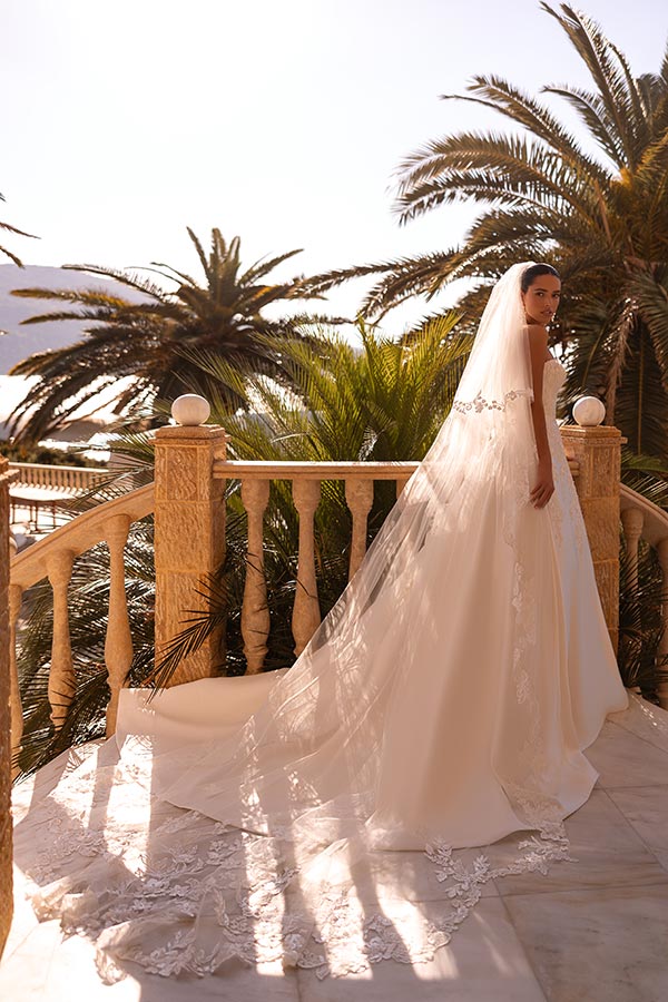 Eine Frau im weißen Brautkleid mit langem Schleier steht lächelnd auf einer Terrasse