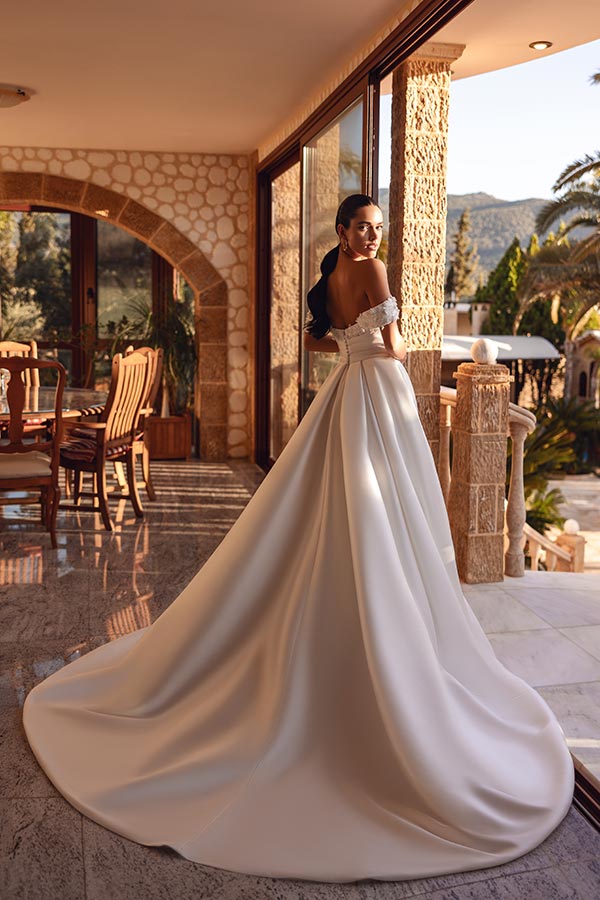 Eine elegante Frau im weißen Brautkleid blickt mit sanftem Lächeln über die Schulter