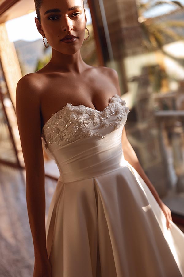 Eine Frau mit ernster Miene trägt ein elegantes weißes trägerloses Brautkleid