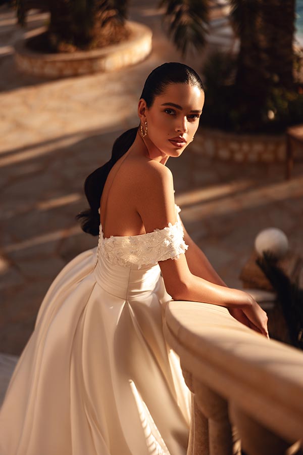 Eine elegante Frau mit langem dunklem Haar trägt ein cremeweißes Brautkleid und schaut nachdenklich