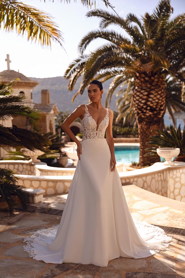 Eine junge Frau mit ernstem Blick trägt ein elegantes weißes Brautkleid im Garten