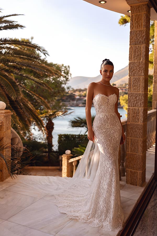 Eine Frau mit ernstem Blick trägt ein elegantes weißes Spitzenkleid auf einer Terrasse