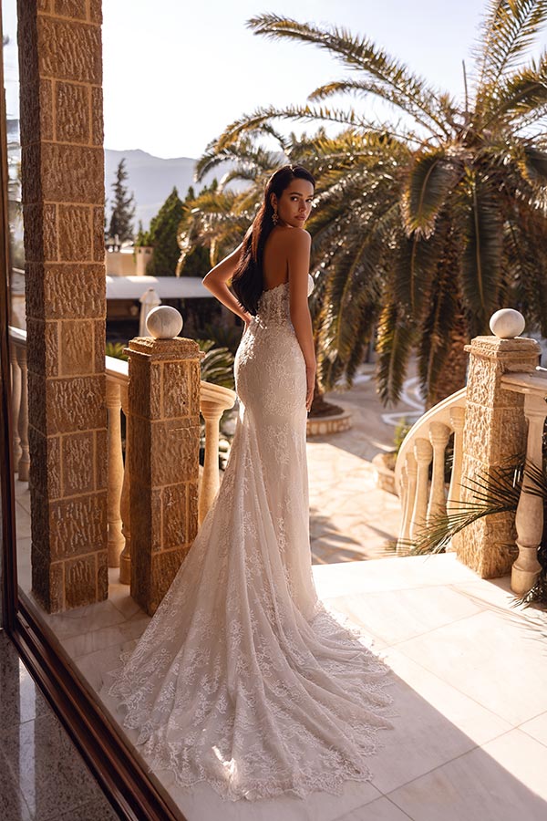 Eine Frau im eleganten weißen Brautkleid steht auf einer Sonnenterrasse und blickt zurück