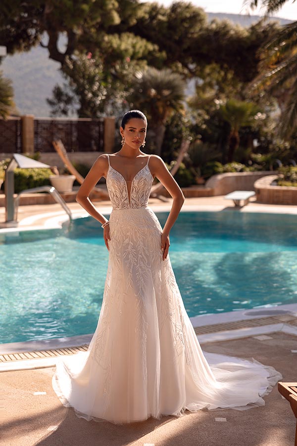 Eine elegant gekleidete Frau in weißem Brautkleid steht selbstbewusst am Pool