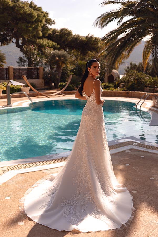 Junge Frau mit ernstem Blick in weißem Spitzenkleid steht elegant am Pool im Sonnenschein