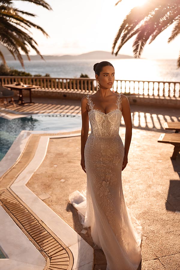 Eine elegante Frau im weißen Spitzenkleid blickt ernst vor Pool und Meer im Sonnenlicht