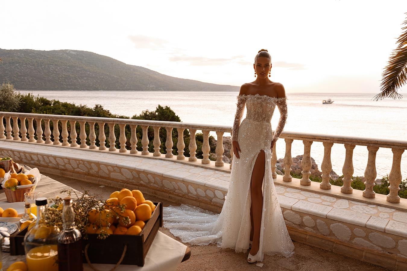 Eine Frau im eleganten weißen Kleid mit Glitzer steht ernst am Meer bei Sonnenuntergang