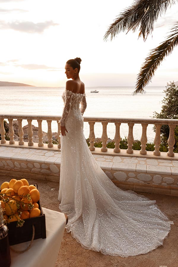 Eine elegant gekleidete Braut im funkelnden weißen Kleid blickt verträumt aufs Meer