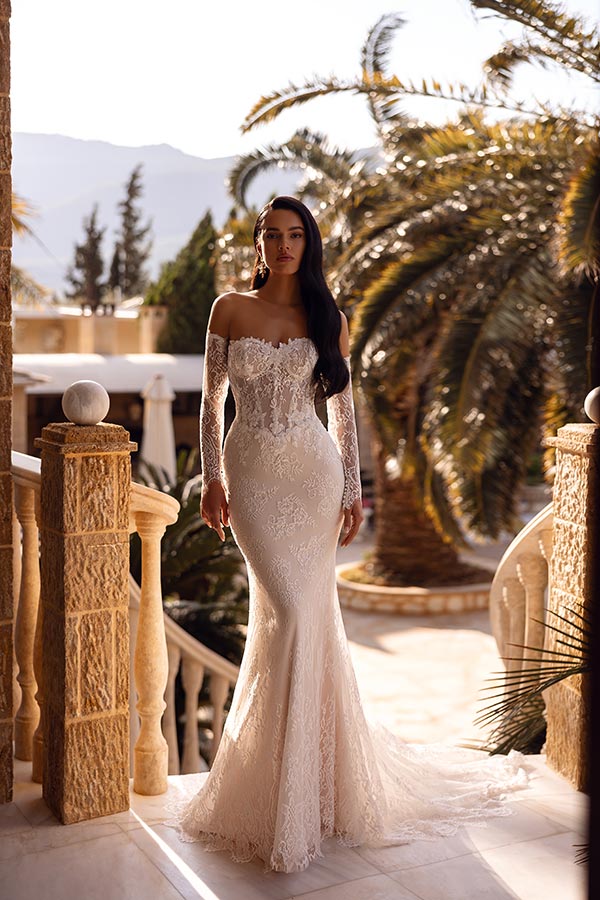 Eine junge Frau im cremefarbenen Spitzenkleid steht stilvoll auf einer sonnigen Terrasse