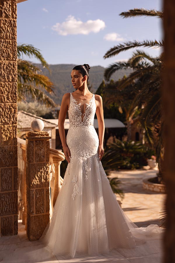 Eine elegante Frau in weißem Spitzenkleid steht auf einer sonnigen Steinterrasse