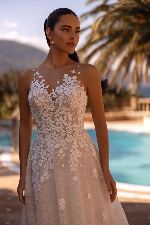 Junge Frau mit ernstem Blick trägt cremefarbenes Kleid mit floraler Spitze am Pool