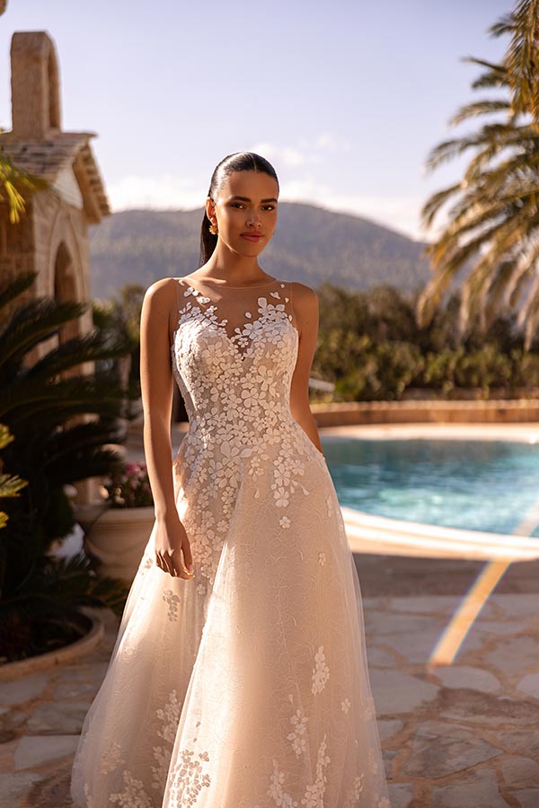 Eine junge Frau mit ernstem Gesicht trägt ein elegantes, cremefarbenes Spitzenkleid am Pool
