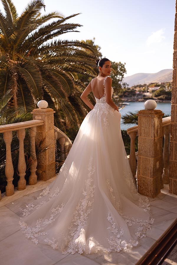 Eine Frau im weißen Spitzenkleid blickt lächelnd über eine mediterrane Terrasse