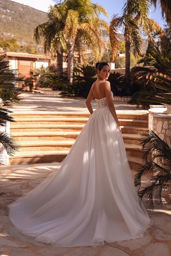 Eine Frau im weißen Brautkleid blickt elegant über die Schulter auf sandfarbenen Stufen