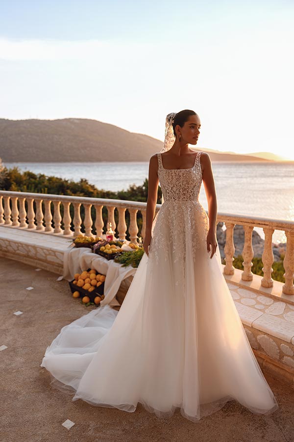 Eine Frau im weißen Brautkleid steht entspannt auf einer Terrasse mit Seeblick im Abendlicht