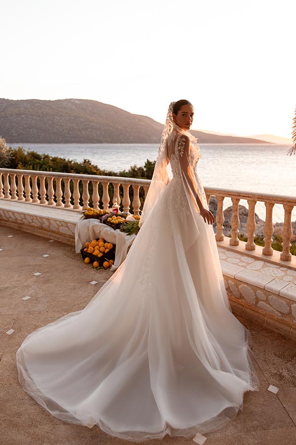 Eine Braut im eleganten weißen Kleid blickt ernst zurück vor Meereskulisse im Sonnenlicht