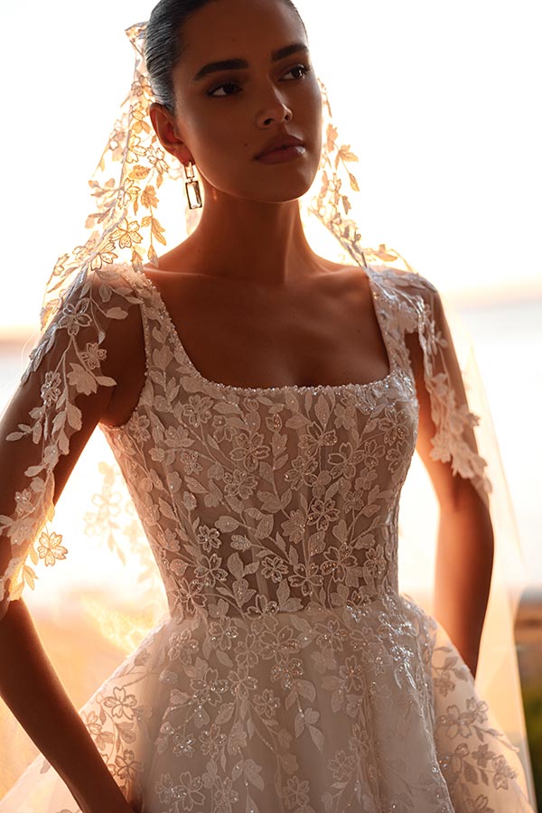 Eine junge Frau mit ernstem Blick trägt ein elegantes, spitzenbesetztes Brautkleid in Weiß