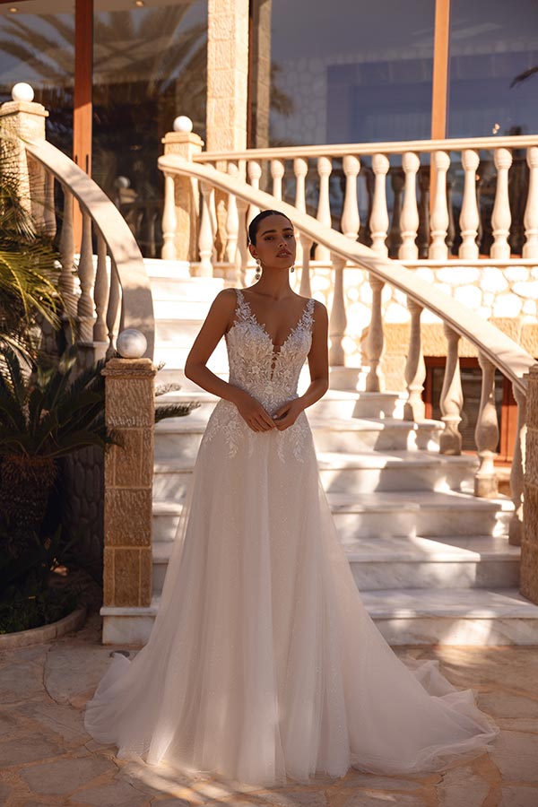 Eine junge Frau im eleganten weißen Brautkleid steht vor einer Steintreppe und blickt verträumt