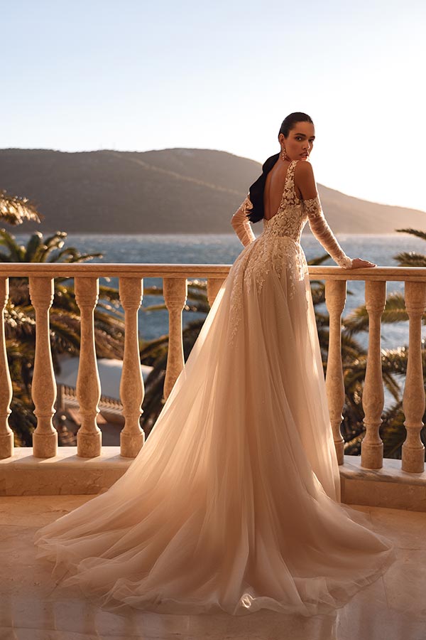 Eine Frau im eleganten cremefarbenen Hochzeitskleid blickt ernst aufs Meer