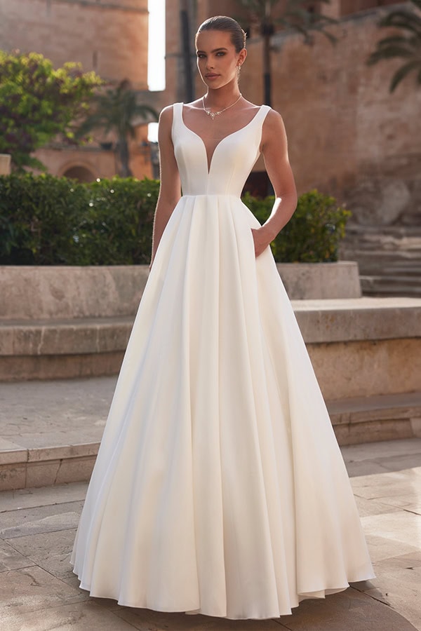 Eine elegante Frau im weißen Brautkleid mit V-Ausschnitt steht selbstbewusst draußen