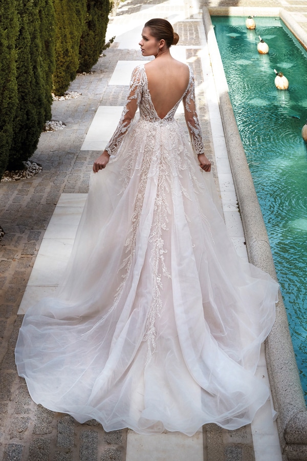 Eine Frau mit Hochsteckfrisur trägt ein elegantes, cremefarbenes Brautkleid mit Rückenausschnitt